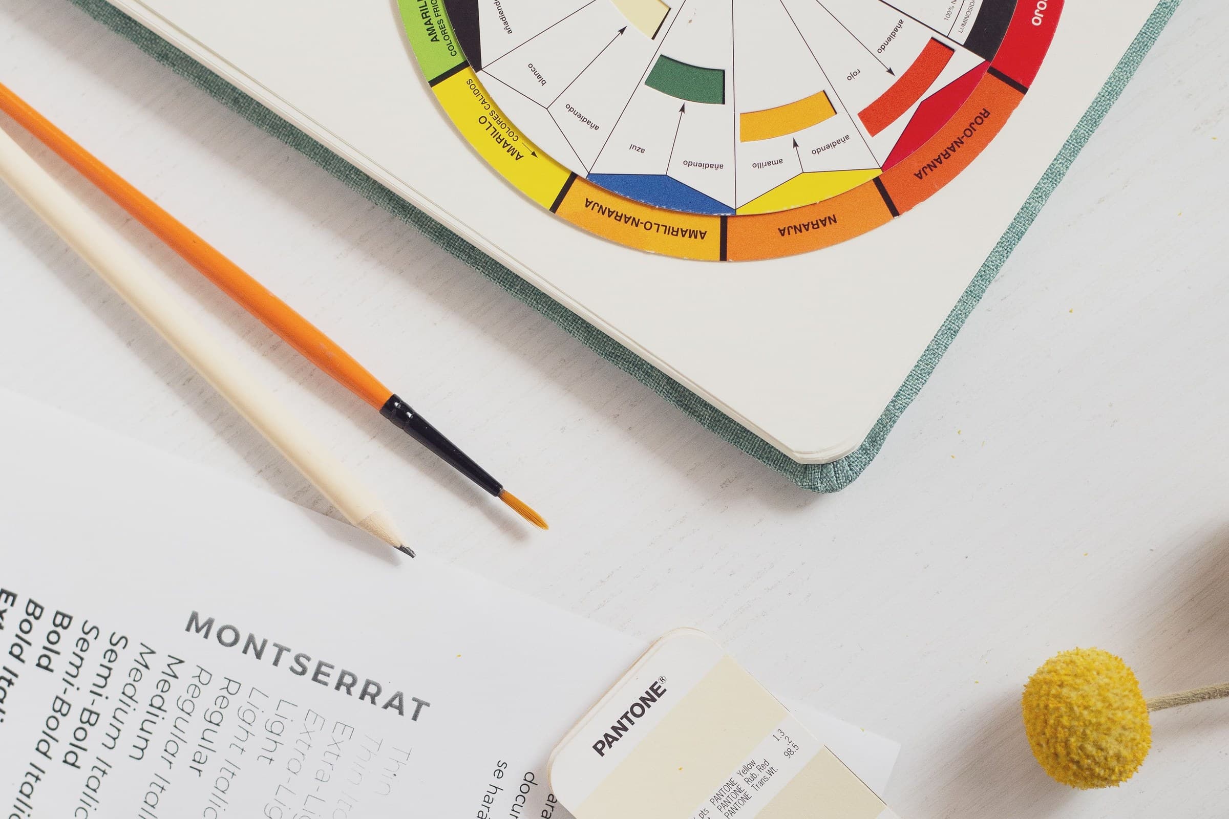 A designer's colour-study desk with a colour wheel, brushes, Pantone chips and a type specimen.