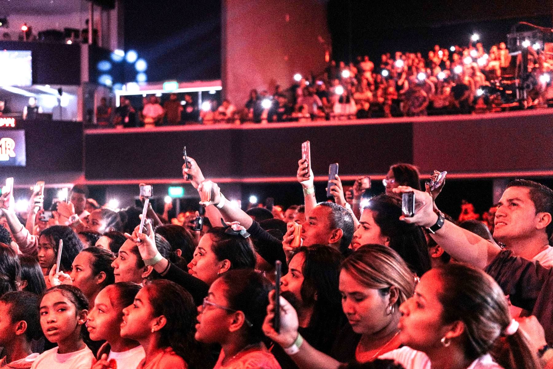 A concert crowd with phones raised toward a lit stage.