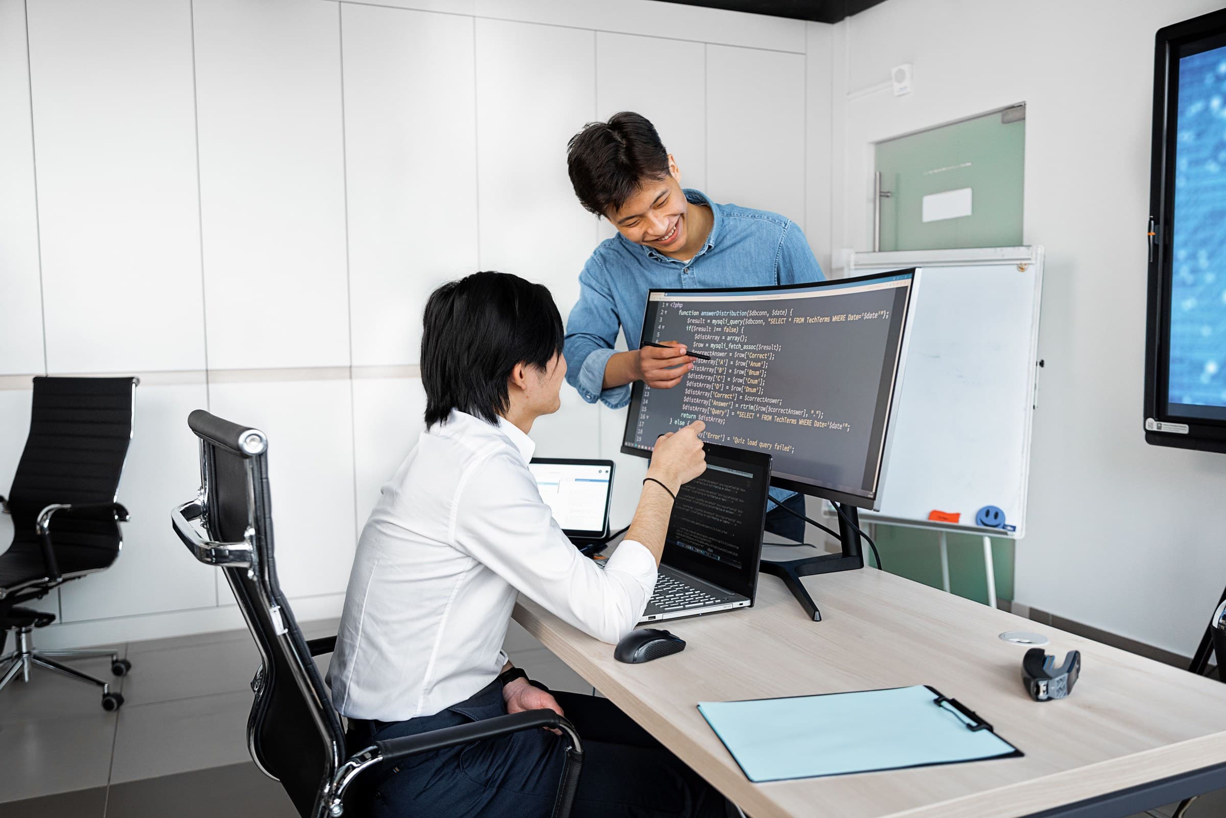 Two developers at a shared desk with source code open on both monitors.
